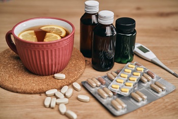 A comforting scene of health and wellness, featuring a warm cup of tea with lemon slices surrounded by various medicines and supplements. This setup evokes a sense of care, reminding us to prioritize our well-being.